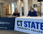 CTECS' Executive Director Dr. Alice Pritchard and CT State's President Royal sit at two tables and sign the agreement