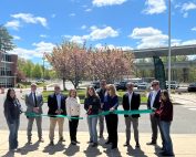 Students from Howell Cheney Technical High School cut the ribbon on the new carport solar energy system (in background), joined by Principal David Batch, DAS Commissioner Michelle Gilman, CTECS Executive Director Dr. Alice Pritchard, and project partners from the Connecticut Green Bank and Verogy.